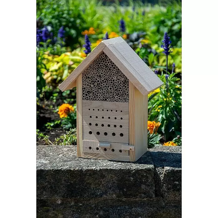 Dobar Bienenhaus Maja - L x B x H: 22,5 x 14 x 29,5 cm, Kiefer - Hölzernes Insektenhotel mit Bambusröhren und Bohrlöchern, auf einer Steinmauer in einem sonnigen Garten.