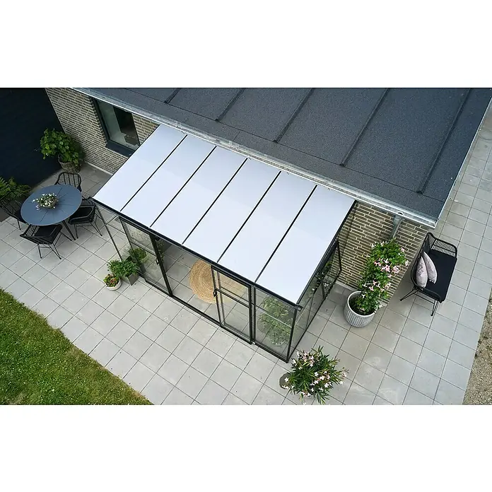 Halls Gewächshaus Qube Lean-to 612Außenmaß inkl. Dachüberstand (B x T): 374 x 188 cm, Material Seitenwand: Glas, 3 mm, Schwarz - Luftaufnahme eines Gewächshauses mit klarem Glas und weißem Dach, umgeben von Pflanzen, Möbeln und einem gepflasterten Gartenbereich.