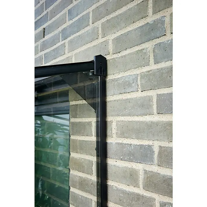 Halls Qube Gewächshaus Lean-to 24 - Außenmaß inkl. Dachüberstand (B x T): 127 x 65 cm, Material Seitenwand: Glas, 3 mm, Schwarz - Nahaufnahme eines schwarzen Fensterrahmens mit Glas vor einer grauen Backsteinmauer, der eine moderne und stilvolle Ästhetik bietet.