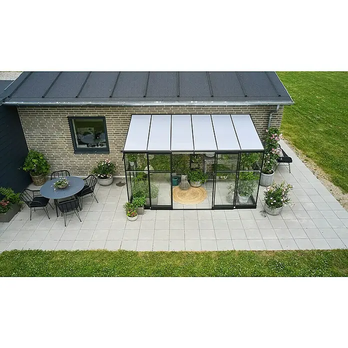 Halls Qube Gewächshaus Lean-to 612 - Außenmaß inkl. Dachüberstand (B x T): 374 x 188 cm, Material Seitenwand: Glas, 3 mm, Schwarz - Ein elegantes Gewächshaus aus Glas und Metall steht auf einer Terrasse, umgeben von Pflanzen und Gartenmöbeln.