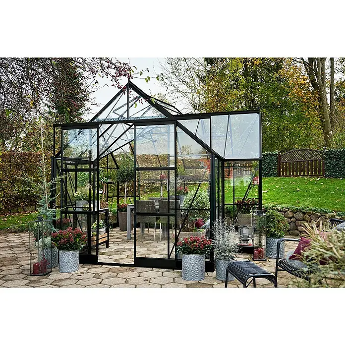 Halls Gewächshaus Garden Room - Außenmaß inkl. Dachüberstand (B x T): 262 x 381 cm, Material Seitenwand: Glas, 3 mm, Schwarz - Elegantes Gewächshaus mit schwarzen Rahmen und Glaswänden, umgeben von einem üppigen Garten mit Blumen und Sträuchern.
