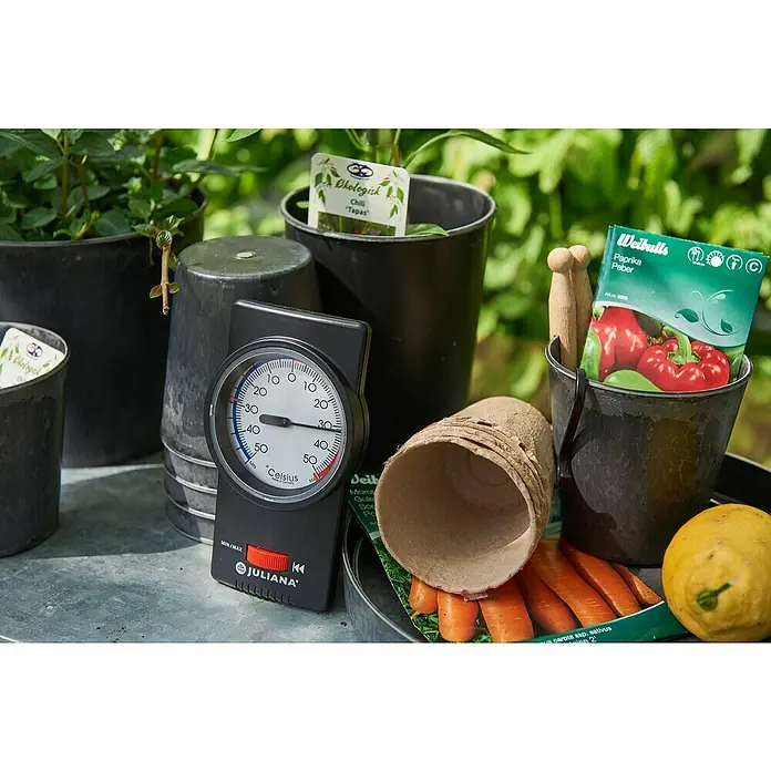 Juliana Thermometer - L x B x H: 20 x 11 x 4,2 cm, Schwarz - Nahaufnahme einer Gartenszene mit Juliana-Thermometer, Pflanzgefäßen und Samenpackungen, die die Freude am Gärtnern und die Werkzeuge für den Erfolg zeigt.
