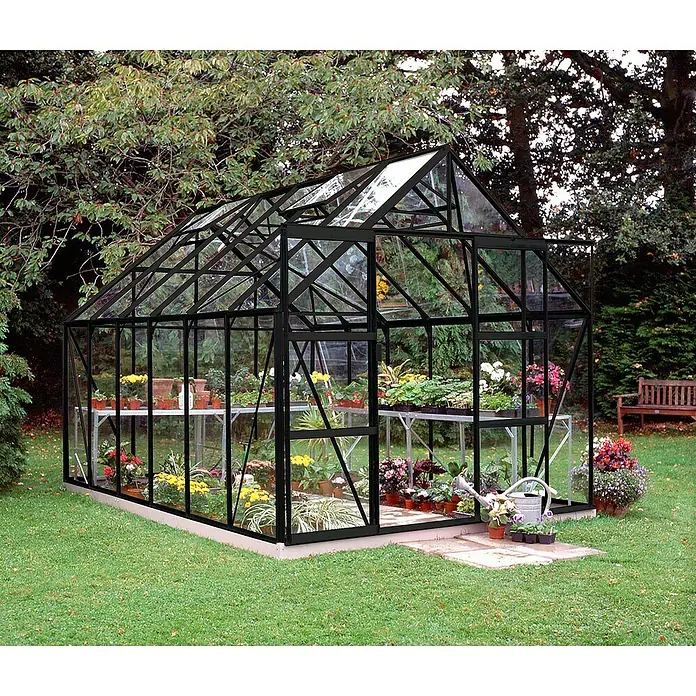 Halls Gewächshaus Magnum 128 - Außenmaß inkl. Dachüberstand (B x T): 257 x 384 cm, Einscheibensicherheitsglas, 3 mm, Schwarz - Ein Gewächshaus mit schwarzem Rahmen, gefüllt mit blühenden Pflanzen auf Tischen, im Garten.