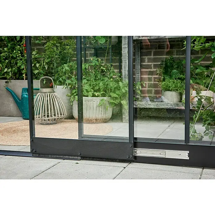 Halls Gewächshaus Qube Lean-to 68 - Außenmaß inkl. Dachüberstand (B x T): 251 x 188 cm, Material Seitenwand: Glas, Schwarz - Detailaufnahme einer Glasschiebetür mit schwarzem Rahmen, die einen Blick in ein Gewächshaus mit Pflanzen und Dekorationen freigibt.