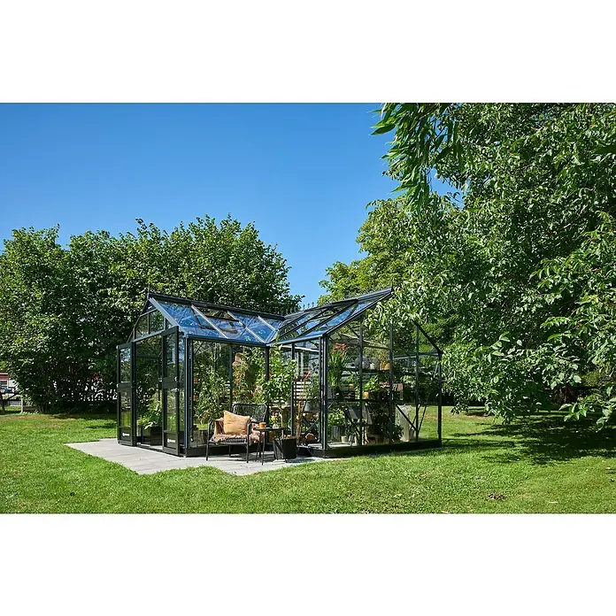 Juliana Gewächshaus Orangerie - Außenmaß inkl. Dachüberstand (B x T): 583 x 439 cm, Material Seitenwand: Glas, 3 mm, Anthrazit/Schwarz - Ein modernes Gewächshaus mit Glaswänden und schwarzem Rahmen auf einem Rasen, umgeben von Bäumen, bietet Platz für Pflanzen und Entspannung.