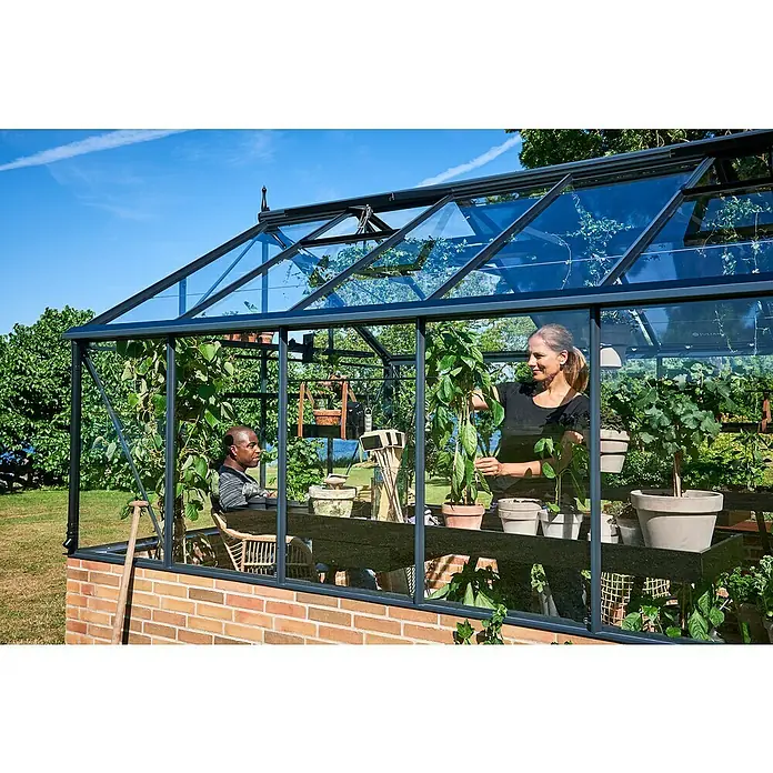 Gewächshaus Premium - Außenmaß inkl. Dachüberstand (B x T): 296 x 439 cm, Material Seitenwand: Glas, Anthrazit/Schwarz - Ein Gewächshaus mit Pflanzen und Personen, das zum Anbau und zur Entspannung im eigenen Garten einlädt.