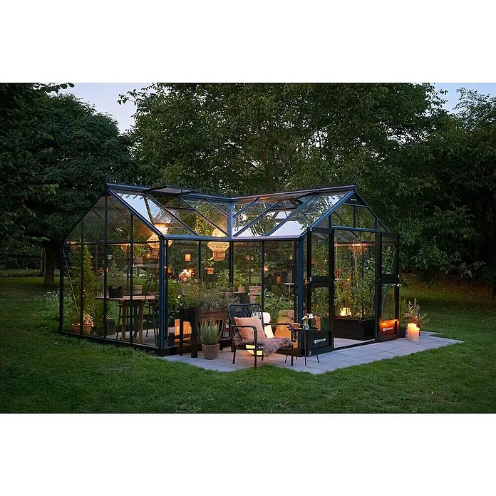Juliana Gewächshaus Orangerie - Außenmaß inkl. Dachüberstand (B x T): 583 x 439 cm, Material Seitenwand: Glas, 3 mm, Anthrazit/Schwarz - Ein elegantes Gewächshaus von Juliana mit Glaswänden und schwarzem Rahmen, beleuchtet und eingerichtet mit Pflanzen und Möbeln.