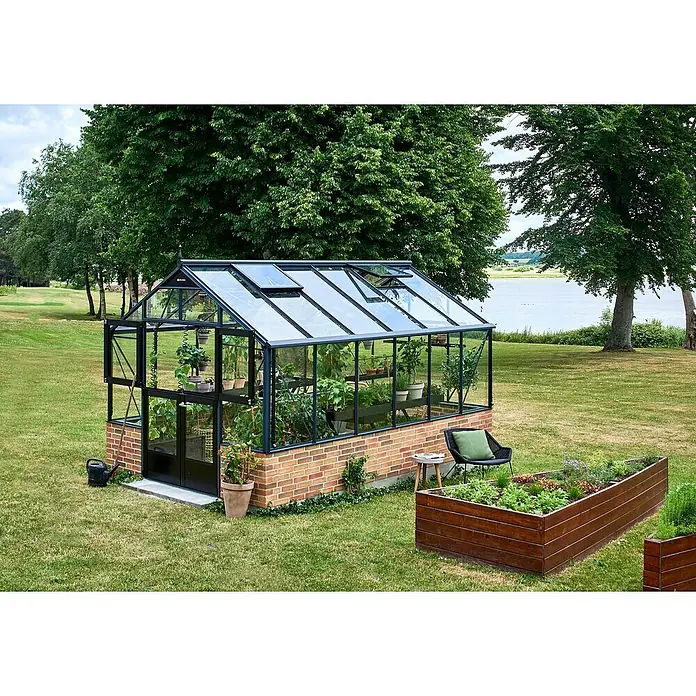 Gewächshaus Premium - Außenmaß inkl. Dachüberstand (B x T): 296 x 439 cm, Material Seitenwand: Glas, Anthrazit/Schwarz - Ein stilvolles Gewächshaus aus Glas und Backstein mit Pflanzen darin, umgeben von einem üppigen Garten mit Bäumen und Rasen.