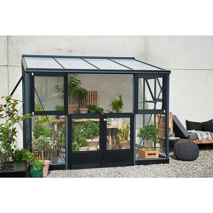 Juliana Gewächshaus Veranda - Außenmaß inkl. Dachüberstand (B x T): 221 x 296 cm, Material Seitenwand: Glas, 3 mm, Anthrazit - Nahaufnahme eines Gewächshauses mit Pflanzen und Kräutern in Töpfen, daneben eine Sitzecke mit Kissen.