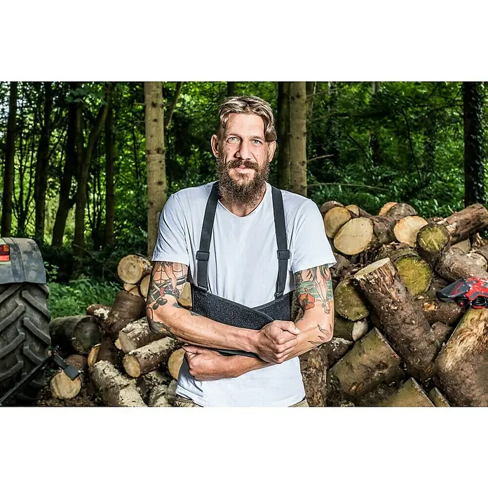 Kneetek Rückenstützgurt BR 108 - XXL, Umfang: 110 m - 138 m - Ein Mann mit Tätowierungen und einer Rückenstütze steht vor einem Holzstapel, neben einem Traktor, im Wald.