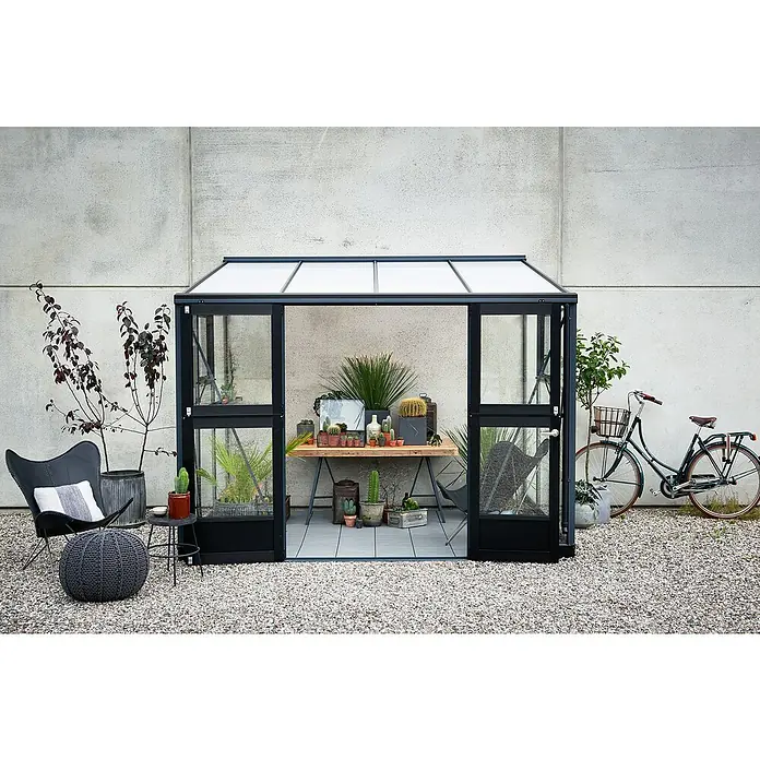 Juliana Gewächshaus Veranda - Außenmaß inkl. Dachüberstand (B x T): 221 x 296 cm, Material Seitenwand: Glas, 3 mm, Anthrazit - Ein modernes Gewächshaus mit schwarzem Rahmen, gefüllt mit Pflanzen, neben einem Fahrrad und einem Sessel. Ideal für Gartenliebhaber.