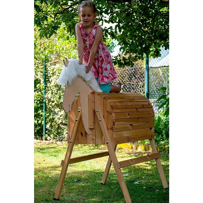 Dobar Holzpferd Bravido - L x B x H: 139 x 78 x 146 cm, Altersempfehlung: 3 Jahre - Ein Mädchen reitet auf einem hölzernen Spielzeugpferd im Garten, umgeben von üppigem Grün.