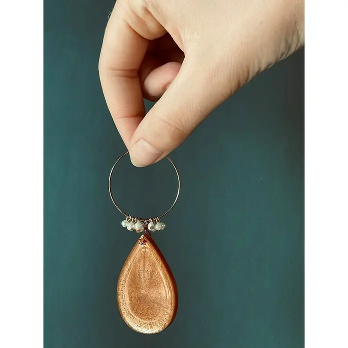 Fleur Resina epoxi Super Transparente - 3,8 l, Transparente - Un primer plano de un pendiente de madera con forma de lágrima sostenido por una mano muestra la intrincada artesanía y la belleza natural.