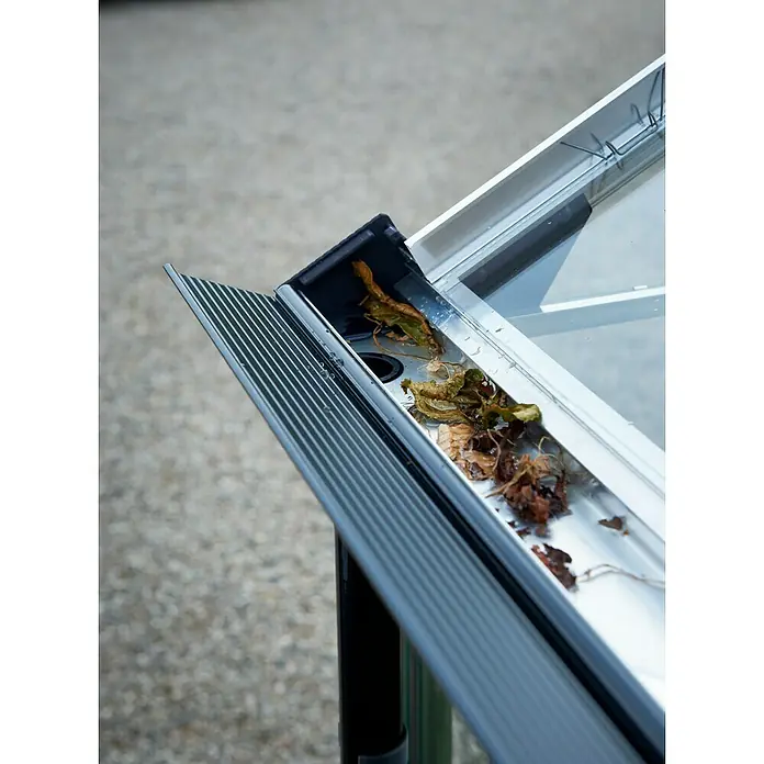 Juliana Gewächshaus Gärtner - Außenmaß inkl. Dachüberstand (B x T): 368 x 439 cm, Material Seitenwand: Glas, 3 mm, Silber/Schwarz - Nahaufnahme einer Dachrinne, die mit Blättern und Schmutz verstopft ist, was die Notwendigkeit regelmäßiger Reinigung hervorhebt.