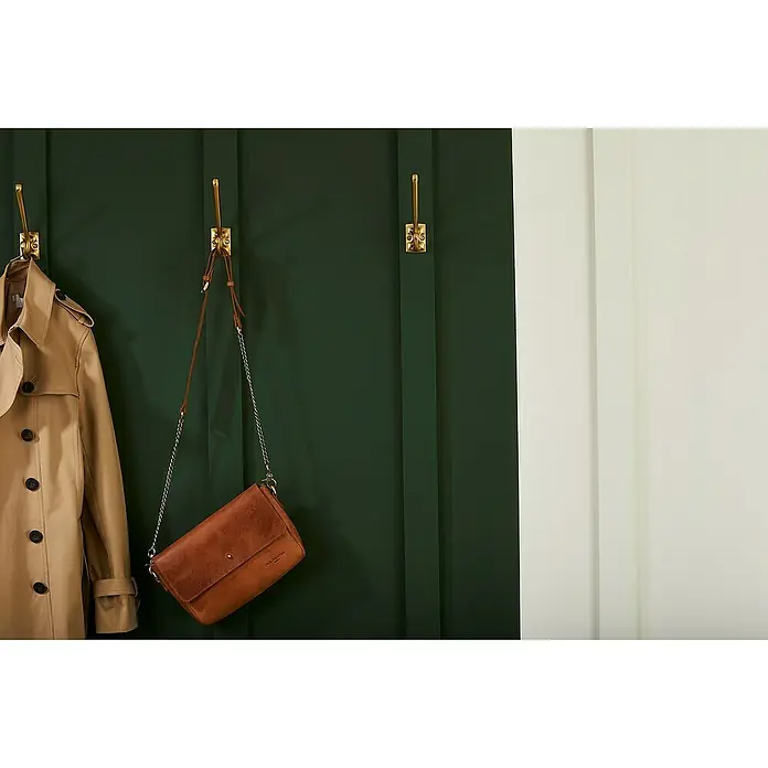 Nmc Decoflair Wandleiste WD2 - 2 m x 15 mm x 70 mm, Hochverdichtetes extrudiertes Polymer (HDPS) - An einer grünen Wand hängen eine braune Handtasche und ein beiger Trenchcoat an goldenen Haken. Die perfekte Kombination für den stilvollen Auftritt.