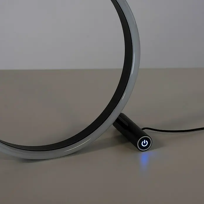 Just Light LED-Tischleuchte RITUS - 13,5 W, Ø x H: 28,5 x 28,5 cm, Anthrazit, Warmweiß - Nahaufnahme einer modernen, kreisförmigen LED-Tischleuchte mit blau leuchtendem Netzschalter auf einem Tisch.