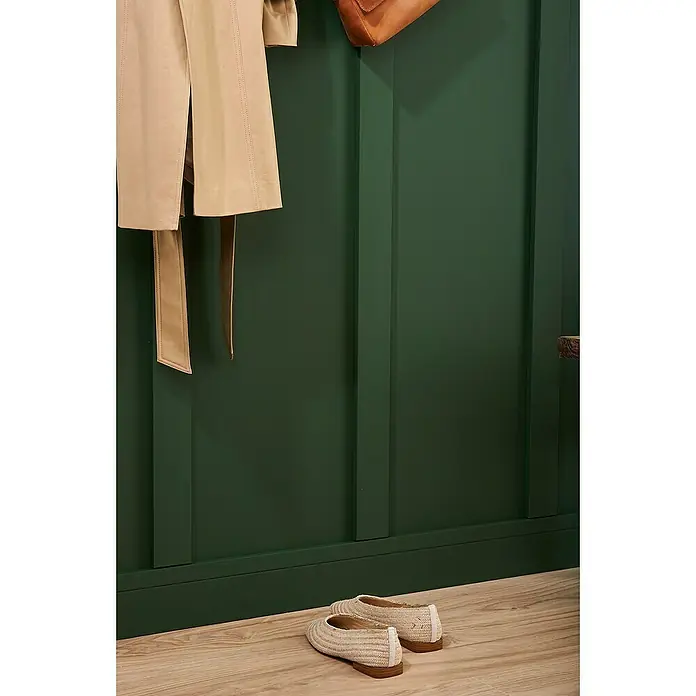 Nmc Decoflair Sockelleiste FD2 - 2 m x 15 mm x 110 mm, Hochverdichtetes extrudiertes Polymer (HDPS) - Ein Paar beigefarbene Ballerinas stehen auf einem Holzboden vor einer dunkelgrünen Wand. Dazu eine passende Jacke und Tasche an der Wand.