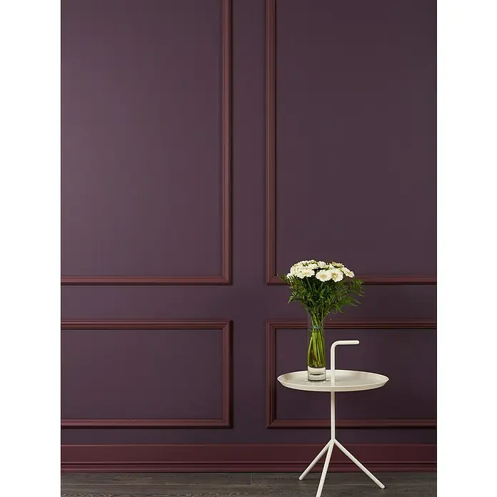 Nmc Decoflair Wandleiste WL2 - 2 m x 20 mm x 40 mm, Hochverdichtetes extrudiertes Polymer (HDPS) - Wandpaneele in Pflaumenfarbe mit schlankem, weißem Beistelltisch und Blumen in einer Vase. Edles Ambiente für stilvolle Räume.