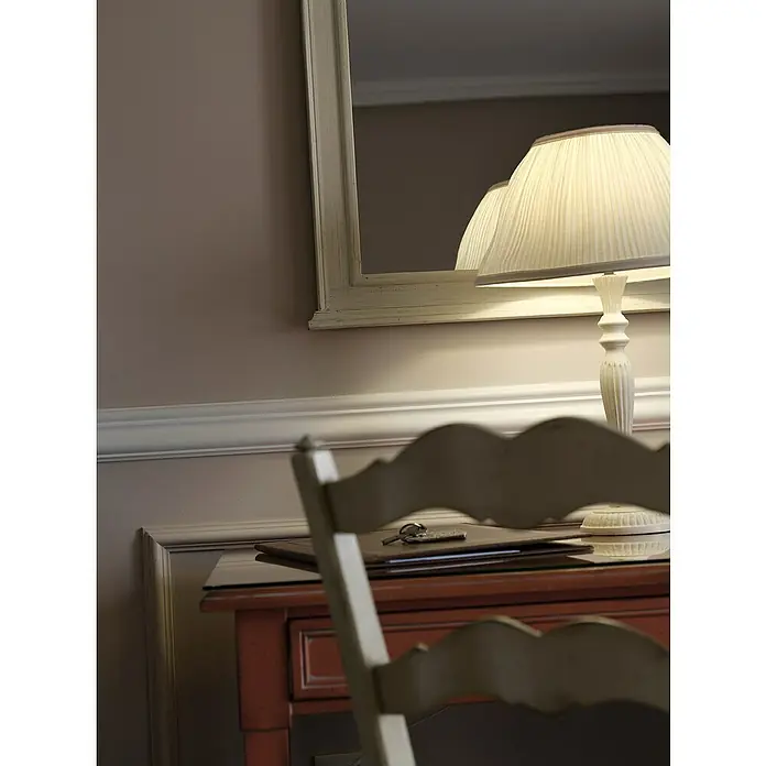 Nmc Decoflair Wandleiste Z13 - 2 m x 22 mm x 80 mm, Hochverdichteter Polyurethanschaum (PU) - Eine Nahaufnahme eines Schreibtisches mit einer Lampe und einem Spiegel. Die Lampe mit weißem Lampenschirm spendet warmes Licht.