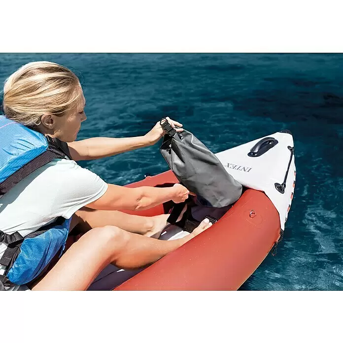 Intex Kajak Komplettset Excursion Pro - Nutzlast: 180 kg, Geeignet für: 2 Personen - Person legt grauen Dry Bag in aufblasbares Kajak auf blauem Wasser.