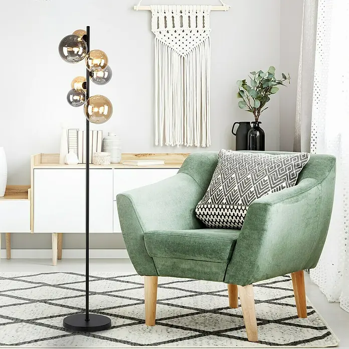 Paul Neuhaus Popsicle Stehleuchte - 21 W, Höhe: 155 cm, Schwarz, G9 - Elegante Stehlampe mit mehreren Kugeln in Gold- und Grautönen. Sie steht neben einem grünen Sessel mit gemustertem Kissen auf einem geometrischen Teppich.