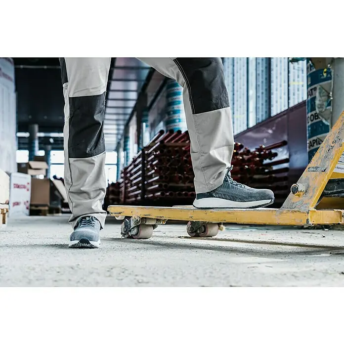 Zapato bajo de seguridad Mauro - 43, Clase de protección según EN ISO 20345: S1P, Gris - En la imagen se muestran zapatos de seguridad Puma, colocados sobre una plataforma de rodillos amarilla. Los zapatos son grises con suela blanca.