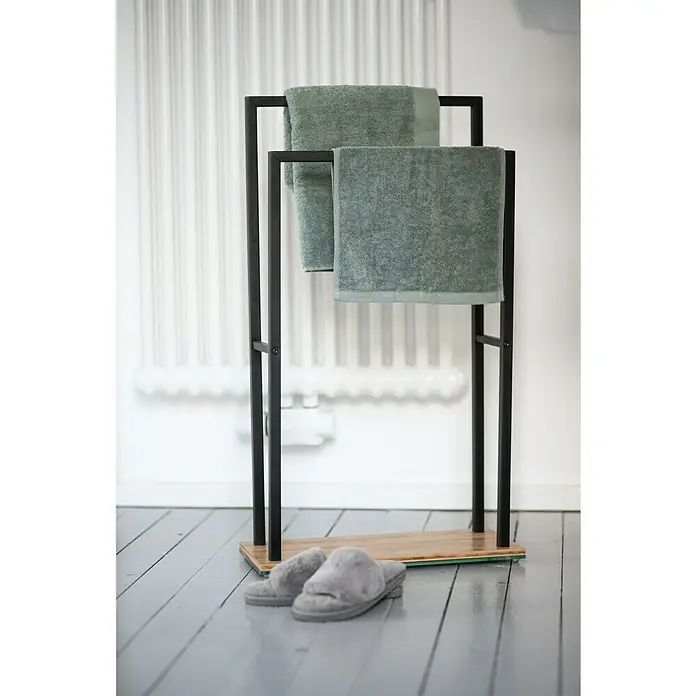 Wenko Toallero de barra Bambusa - L x An x Al: 20 x 46 x 80 cm, Acero, Negro - Toallero con dos toallas verdes y zapatillas grises sobre un suelo de madera gris.