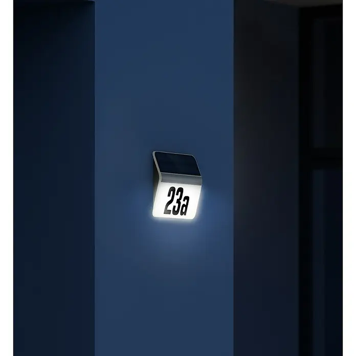 Steinel XSolar Solar-Hausnummer LH-N Edelstahl - IP44, Edelstahl - Eine quadratische Hausnummerleuchte mit der Nummer 23a, die an einer blauen Wand befestigt ist und einladendes Licht ausstrahlt.