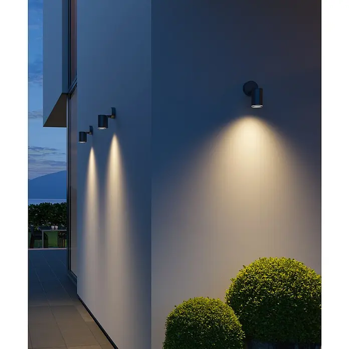 Steinel LED-Außenstrahler Spot One anthrazit - 6,7 W, L x B x H: 9,8 x 9,7 x 17,5 cm, Anthrazit, IP44 - Fassadenbeleuchtung mit modernen Wandleuchten, die warmes Licht auf die Hauswand und die gepflegten Büsche werfen.