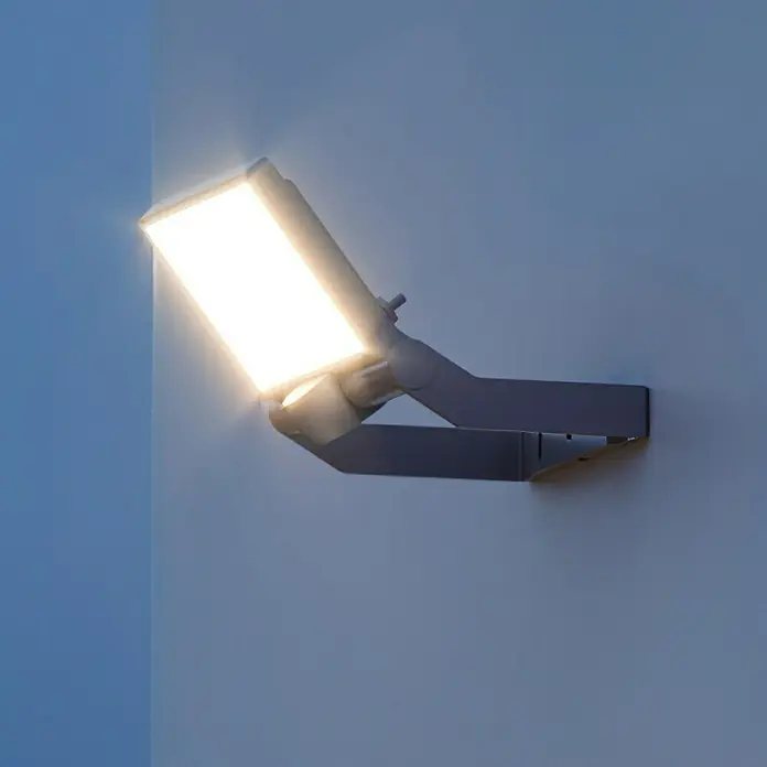 Steinel Proyector LED XLED ONE - 17,8 W, L x An x Al: 17,3 x 22,9 x 19,5 cm, Acero inoxidable, Blanco cálido - Primer plano de una moderna lámpara LED de exterior montada en la pared, que emite una iluminación direccional brillante.