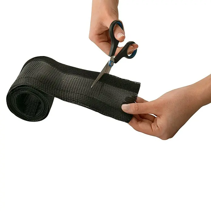 Inofix Organizador de cables de malla expandible - Negro, 8,2 cm x 1,5 m - Imagen de una persona cortando un rollo de material de funda trenzada negra con unas tijeras. Ideal para la gestión y protección de cables.