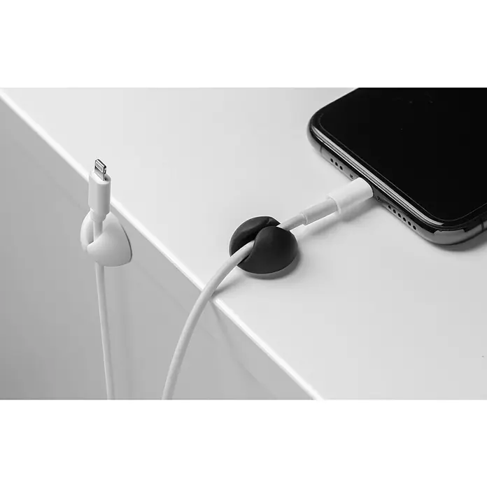 Inofix Fijación para cables adhesivo Mini - Blanco y Negro, 8 ud. - Organizador de cables con un clip negro y uno blanco para una gestión ordenada de los cables en una mesa blanca junto a un smartphone.