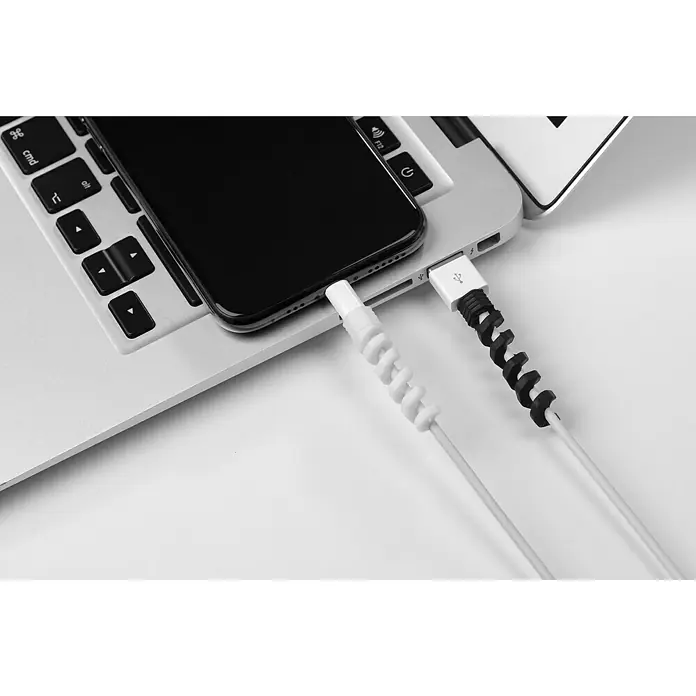 Inofix Protector de cables - Blanco y Negro, 4 ud. - Un smartphone se está cargando en un portátil con dos protectores de cable en espiral, uno negro y otro blanco.