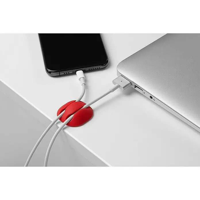 Inofix Fijación para cables adhesivo - Multicolor, 4 ud. - Un organizador de cables rojo sujeta los cables de carga de un teléfono inteligente y un portátil sobre una mesa blanca. Accesorio práctico.