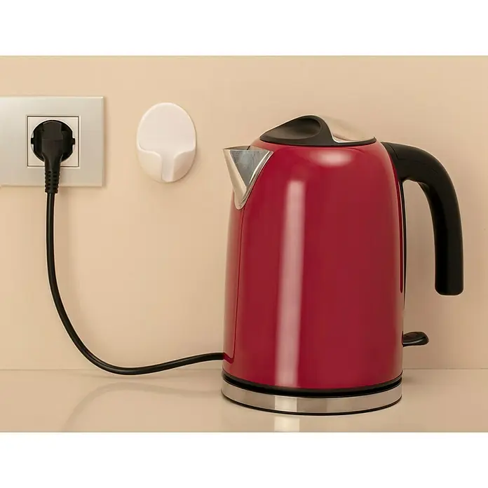 Inofix Colgador adhesivo para enchufes - Plástico, Blanco, 2 ud. - Hervidor rojo sobre una encimera de cocina junto a un enchufe con un enchufe negro enchufado y un soporte blanco en la pared.