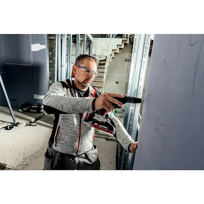 Metabo CAS 18V Akku-Trockenbauschrauber TBS 18 LTX BL 5000 - 18 V, 2 Akkus, 2 Ah - Ein Handwerker befestigt eine Gipskartonplatte mit einem Metabo Akku-Trockenbauschrauber in einem unfertigen Raum.