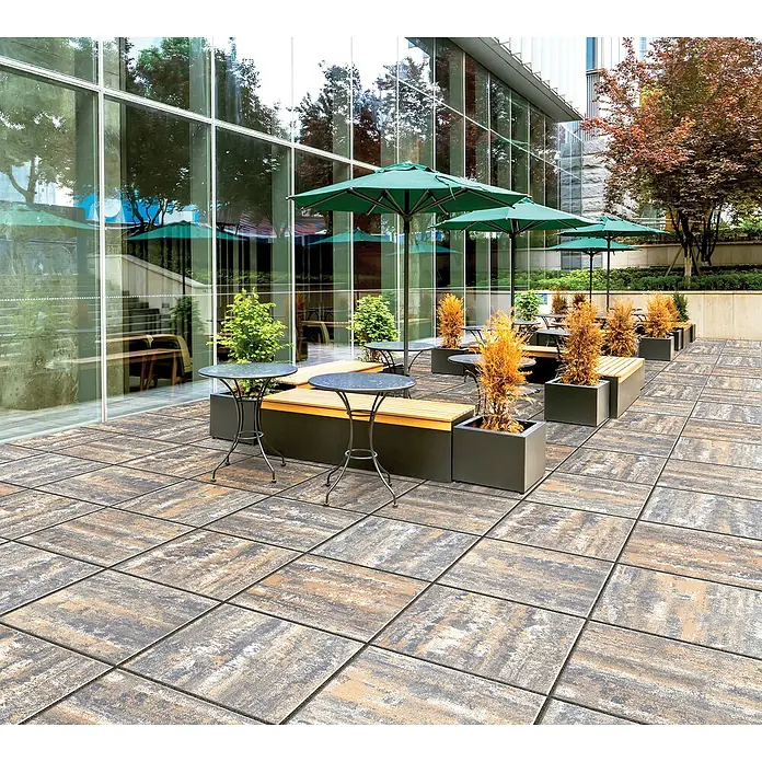 Terrassenplatte Saturn - 50 x 50 x 4 cm, Muschelkalk, Beton - Außenbereich mit eleganten Terrassenplatten, Tischen, Bänken und grünen Sonnenschirmen vor einem modernen Gebäude.