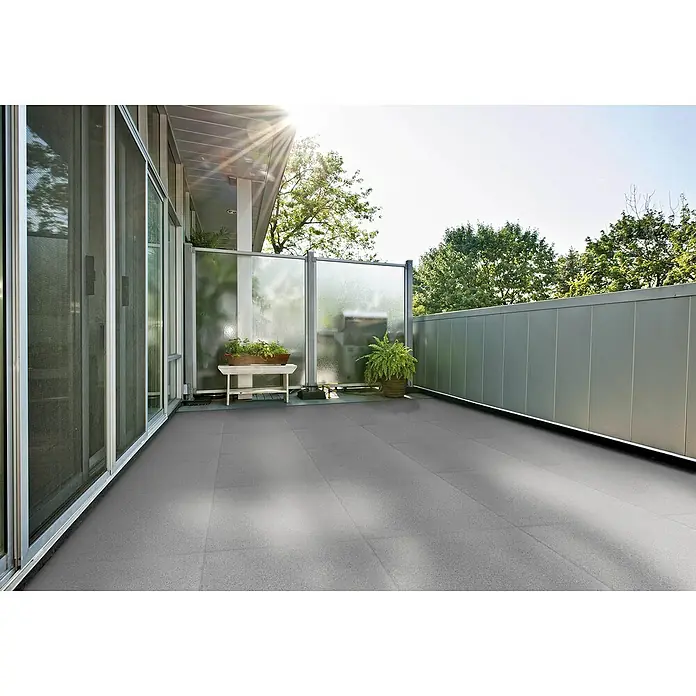 Terrassenplatte Titanio Glatt - 40 x 40 x 4 cm, Grau, Beton - Blick auf eine Terrasse mit grauen Fliesen, einer Glaswand, Pflanzen und einer weißen Bank, die eine gemütliche Atmosphäre erzeugt.