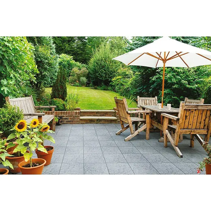 Terrassenplatte Rustica - 40 x 40 x 4 cm, Titanio, Beton - Einladende Gartenszene mit grauen Terrassenfliesen, rustikalen Holzmöbeln und üppiger Bepflanzung, ideal für entspannte Stunden im Freien.
