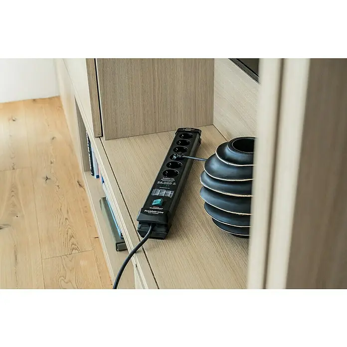 Brennenstuhl Premium-Line Steckdosenleiste - 6-fach, Schwarz, Kabellänge: 1,8 m, IP20, Mit Schalter - Eine schwarze Brennenstuhl Premium-Line Steckdosenleiste mit Überspannungsschutz und ein Deko-Objekt stehen auf einem Regal.