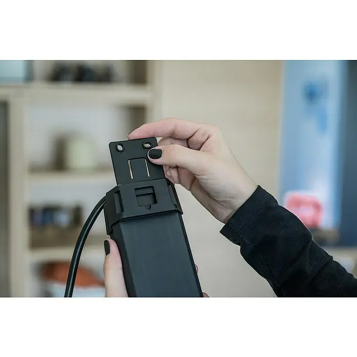 Brennenstuhl Premium-Line Steckdosenleiste - 6-fach, Schwarz, Kabellänge: 1,8 m, IP20, Mit Schalter - Detailaufnahme eines schwarzen Geräts, das von einer Hand mit schwarzen Nägeln zusammengebaut wird, im Hintergrund verschwommene Regale.