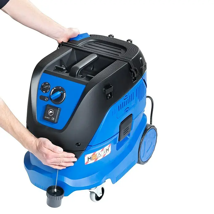 Nilfisk Elektro-Nass- & Trockensauger Attix 33-2M PC - 1.400 W, Behältervolumen: 30 l - Dieser Artikel zeigt einen blauen und schwarzen MEGA M Industriesauger mit Rädern, der von zwei Händen gehalten wird.