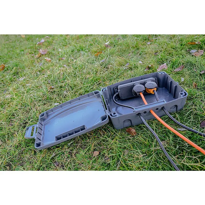 Brennenstuhl Kabelbox - L x B x H: 34 x 23 x 12,5 cm, IP54 - Eine graue Outdoor-Steckdosenbox mit geöffnetem Deckel und mehreren eingesteckten Kabeln auf einer grünen Rasenfläche.