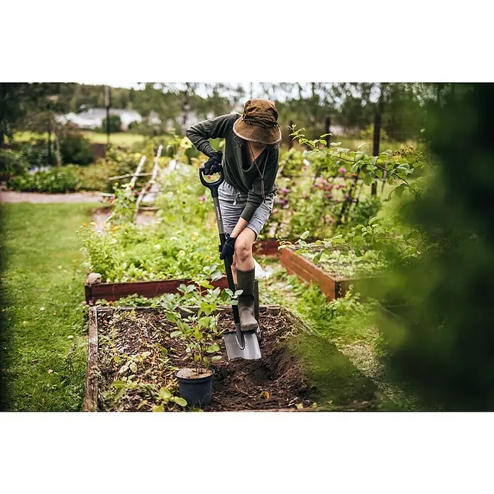 Fiskars Ergonomic Gärtnerspaten - Spitz, 1,25 m - Eine Person benutzt einen Fiskars Spaten im Garten, um ein Loch für eine Pflanze vorzubereiten. Der Spaten sticht sauber in die Erde.
