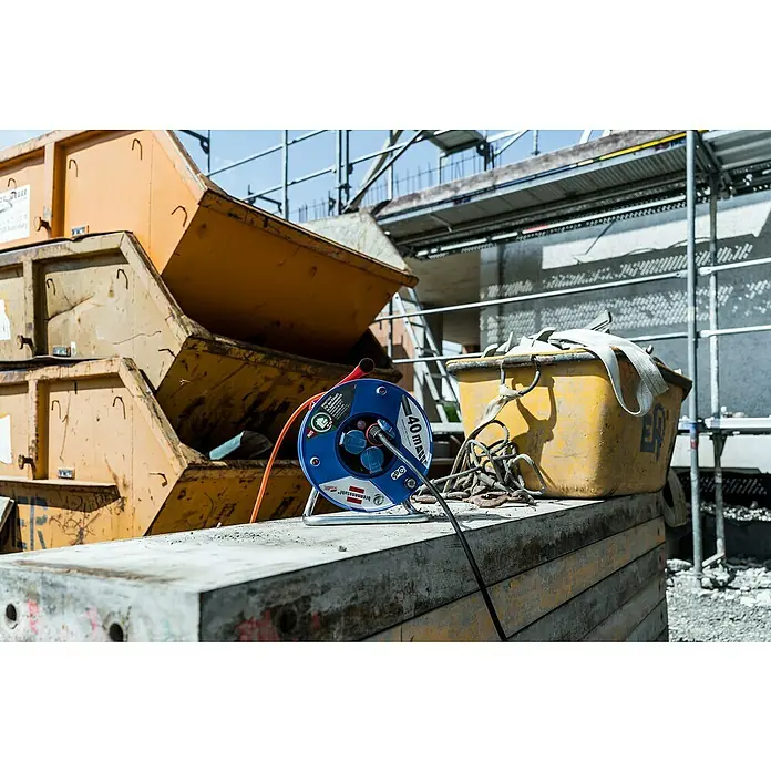 Brennenstuhl Garant Kabeltrommel - Kunststoff, 40 m, AT-N05V3V3-F, IP44 - Blaue Brennenstuhl Kabeltrommel mit Steckdosen auf einer Baustelle, mit orangefarbenem Kabel und gelbem Behälter.