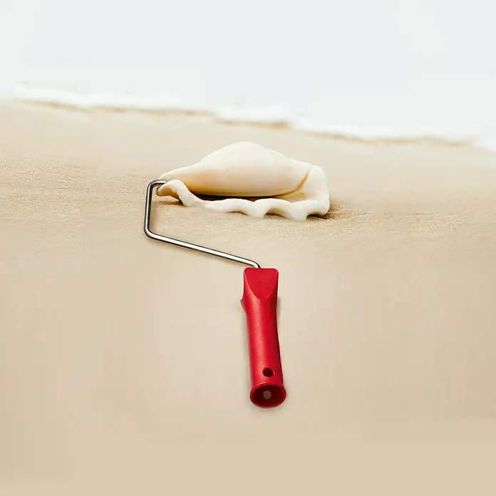 SCHÖNER WOHNEN-Farbe Wandfarbe Trendfarbe - Sand, Matt, 2,5 l, Konservierungsmittelfrei - Nahaufnahme einer Farbwalze, die ein weißes Muschelornament auf beigem Sand bemalt, wodurch eine künstlerische und kreative Komposition entsteht.