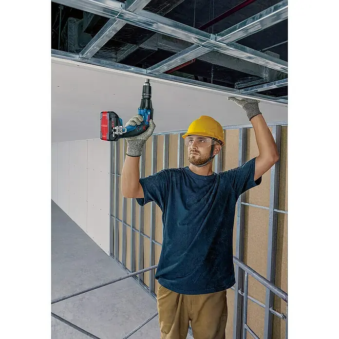 Bosch Professional AMPShare 18V Akku-Trockenbauschrauber GTB 18V-45 - 18 V, 2 Akkus, 6 Nm, Leerlaufdrehzahl 1. Gang: 0 U/min - 4.500 U/min - Ein Bauarbeiter befestigt mit einem blauen Akkuschrauber eine Deckenplatte, geschützt durch Helm und Brille.