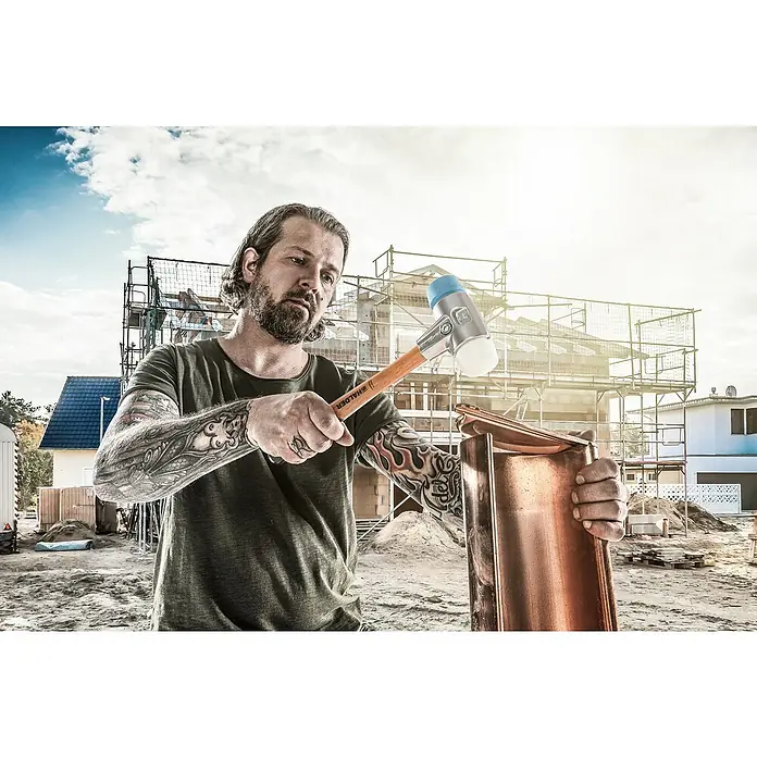 Halder Simplex Schonhammer TPE-Soft / Superplasik - Durchmesser Kopf: 50 mm, Aluminium - Ein Handwerker mit Tätowierungen benutzt einen Halder-Hammer, um ein Metallstück zu bearbeiten, mit einem Baugerüst im Hintergrund.