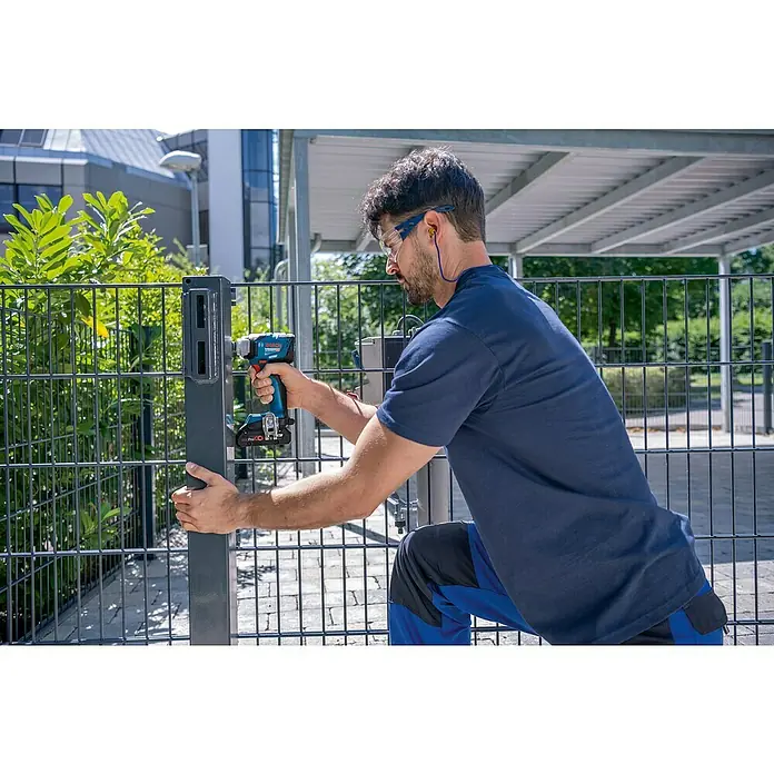 Bosch Professional AMPShare 18V Akku-Drehschlagschrauber GDS 18V-330 HC - 18 V, Ohne Akku, Max. Drehmoment: 330 Nm - Ein Mann befestigt einen Zaunpfosten mit einem blauen Bosch-Akkuschrauber, der Akku ist rot. Er trägt Schutzbrille und Kopfhörer.