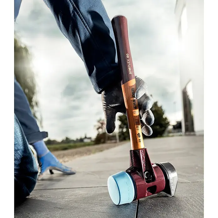 Halder Simplex Schonhammer TPE-Soft mit Standfuß - Durchmesser Kopf: 60 mm - Ein Halder SIMPLEX Schonhammer mit blauem und schwarzem Schlagkopf wird von einer Person auf Pflastersteinen gehalten.